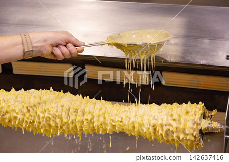 Hand pouring sauce over rotating meat skewer in commercial kitchen setting Hand pouring sauce over rotating meat skewer in commercial kitchen setting 142637416