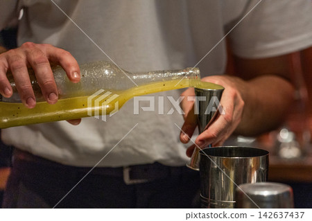 Bartender pouring vibrant cocktail mix into jigger for drink preparation 142637437