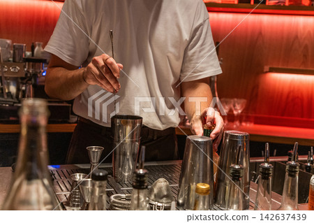 Bartender mixing cocktails at bar with shiny tools and vibrant lighting 142637439