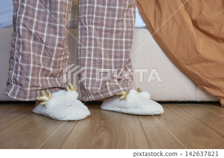 Person standing beside bed wearing pajama pants and soft white slippers Person standing beside bed wearing pajama pants and soft white slippers 142637821