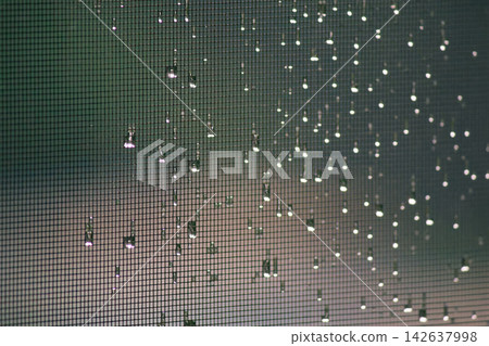 Raindrops and glowing bokeh lights on window screen mesh with green background Raindrops and glowing bokeh lights on window screen mesh with green background 142637998