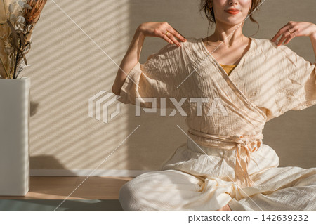 A woman enjoying morning stretches in natural yoga wear; time to soothe mind and body in the sunshine. A woman enjoying morning stretches in natural yoga wear; time to soothe mind and body in the sunshine. 142639232
