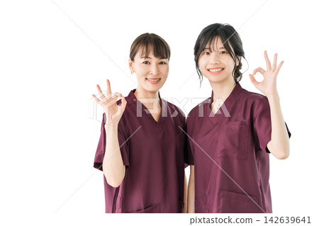 兩名女性醫護人員面帶微笑地比出「OK」手勢。她們身穿手術服的剪影照片,傳遞出一種令人安心和信任的感覺。 兩名女性醫護人員面帶微笑地比出「OK」手勢。她們身穿手術服的剪影照片,傳遞出一種令人安心和信任的感覺。 142639641