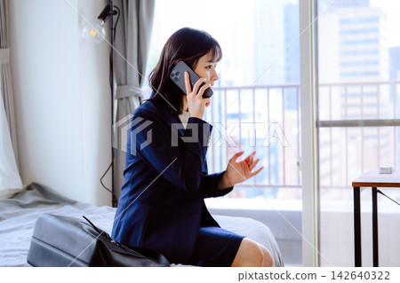 一位身穿西裝的女士正在房間裡打電話;她使用的是智慧型手機。 一位身穿西裝的女士正在房間裡打電話;她使用的是智慧型手機。 142640322