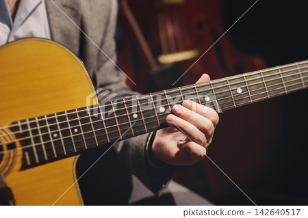 Concert view of acoustic electric guitar player with vocalist and rock band performing in a club, male musician guitarist on stage with audience in a crowded concert club hall arena, hands on guitar Concert view of acoustic electric guitar player with vocalist and rock band performing in a club, male musician guitarist on stage with audience in a crowded concert club hall arena, hands on guitar 142640517
