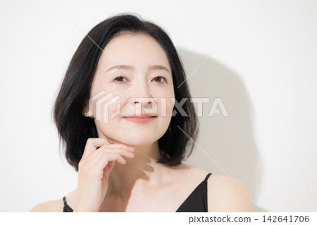 A 50-year-old woman with beautiful, glowing skin and a natural expression smiles directly at the beauty camera; skincare and anti-aging care. A 50-year-old woman with beautiful, glowing skin and a natural expression smiles directly at the beauty camera; skincare and anti-aging care. 142641706