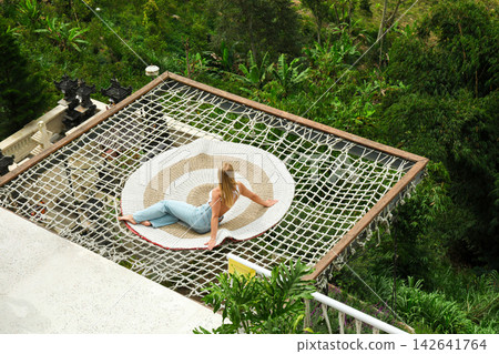 A person rests on a large net with green hills behind them A person rests on a large net with green hills behind them 142641764