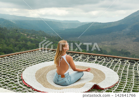 Woman does yoga on a mat with mountains behind her Woman does yoga on a mat with mountains behind her 142641766