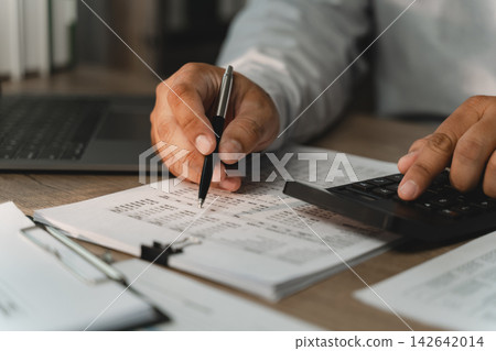Businessman pointing at printed financial documents with pen while using calculator for corporate budgeting, accounting review, revenue analysis, expense 142642014