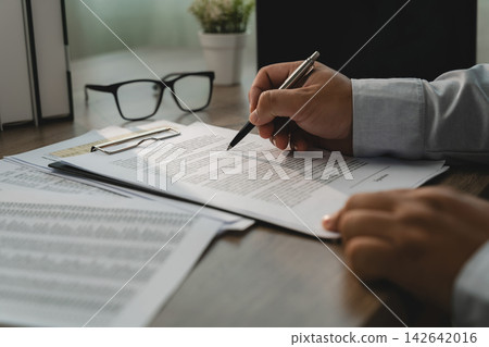 Hands holding a pen over printed agreement 142642016