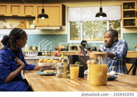 Frustrated boyfriend and girlfriend quarreling over debts and spending, screaming and blaming each other at a kitchen table with bills and receipts. Concerned angry adults with money problems. Frustrated boyfriend and girlfriend quarreling over debts and spending, screaming and blaming each other at a kitchen table with bills and receipts. Concerned angry adults with money problems. 142642050