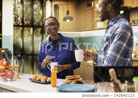 Black lovers chatting in the kitchen over fresh roasted coffee in cups at modern home, discussing about weekend plans and serving healthy breakfast of carbs and proteins. Healthy eating. Black lovers chatting in the kitchen over fresh roasted coffee in cups at modern home, discussing about weekend plans and serving healthy breakfast of carbs and proteins. Healthy eating. 142642125