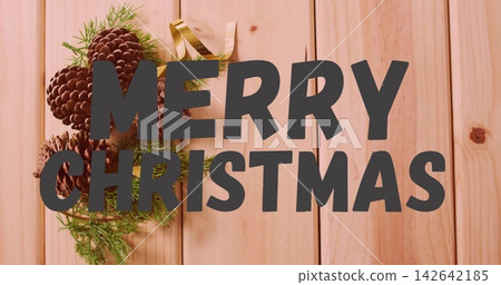 Dominating dark-gray MERRY CHRISTMAS text over pine planks, pine cones, fir sprigs, gold ribbon Dominating dark-gray MERRY CHRISTMAS text over pine planks, pine cones, fir sprigs, gold ribbon 142642185