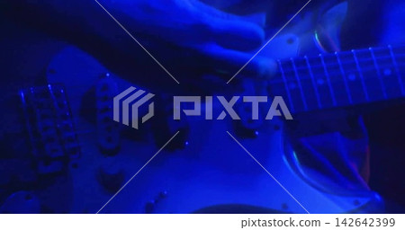 Strumming guitarist hands pressing strings on neck, as blue stage lights coming on, showing pickups Strumming guitarist hands pressing strings on neck, as blue stage lights coming on, showing pickups 142642399