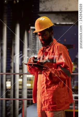 African american environmental engineer uses radio communication to inspect offshore drilling systems, ensuring efficient fuel production and compliance with oil and fuel extraction. 142642689