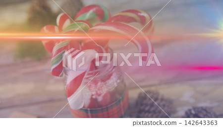 Glass jar wearing lace and plaid ribbon, holding candy canes with pine cones, lens flares Glass jar wearing lace and plaid ribbon, holding candy canes with pine cones, lens flares 142643363