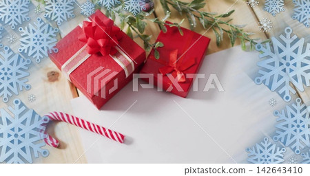 Displaying two red gift boxes on wood tabletop, with candy cane, evergreen sprigs, blue snowflakes 142643410