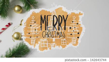 Showing torn orange cutout MERRY CHRISTMAS on gray tabletop, with pine sprigs, gold baubles 142643744