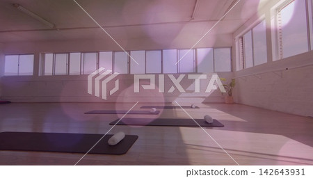 Displaying front yoga mat featuring rolled white towel on wooden floor in studio by long windows Displaying front yoga mat featuring rolled white towel on wooden floor in studio by long windows 142643931