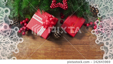 Displaying red box, white ribbon bow, sitting on wood table amid greens, red bead star, snowflakes Displaying red box, white ribbon bow, sitting on wood table amid greens, red bead star, snowflakes 142643969