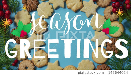 Showing centered wreath of holiday cookies on blue backdrop, featuring white season GREETINGS text Showing centered wreath of holiday cookies on blue backdrop, featuring white season GREETINGS text 142644024
