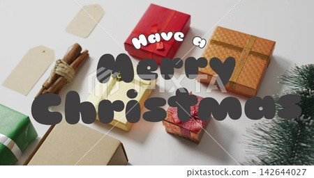Displaying gift boxes with tags, cinnamon and evergreen sprig with greeting text on white tabletop Displaying gift boxes with tags, cinnamon and evergreen sprig with greeting text on white tabletop 142644027