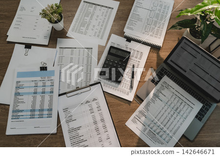 Financial reports, calculator, laptop and accounting documents arranged on office desk for financial report review, data analysis and accounting workflow. Financial reports, calculator, laptop and accounting documents arranged on office desk for financial report review, data analysis and accounting workflow. 142646671