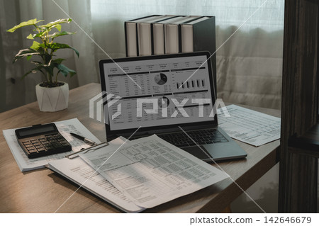 Laptop financial dashboard with calculator and printed reports on office desk for invoice management, receipt accounting, cash flow review, bookkeeping, finance analysis. Laptop financial dashboard with calculator and printed reports on office desk for invoice management, receipt accounting, cash flow review, bookkeeping, finance analysis. 142646679