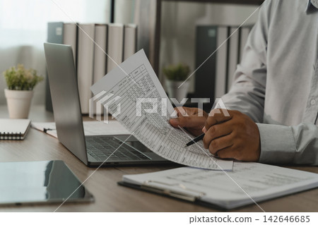 Businessman reviewing payroll report with pen beside laptop for payroll processing, salary calculation, employee records, HR administration, accounting review. 142646685