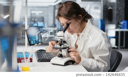 Zoom in on histology technician in lab using scientific microscope for cellular analysis. Woman studies microorganisms inside modern research facility with optical device equipment, camera B Zoom in on histology technician in lab using scientific microscope for cellular analysis. Woman studies microorganisms inside modern research facility with optical device equipment, camera B 142646835