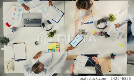 Top down view of associates meeting to review budgeting and resource allocation in a briefing session. Multinational company work team analyzes data for strategic planning. Top down view of associates meeting to review budgeting and resource allocation in a briefing session. Multinational company work team analyzes data for strategic planning. 142646836