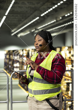 Black call center worker using headset to handle tracking numbers, cargo status and customer complaints. Woman transmitting parcel tracking info for e-commerce delivery services, shipment. Black call center worker using headset to handle tracking numbers, cargo status and customer complaints. Woman transmitting parcel tracking info for e-commerce delivery services, shipment. 142646882