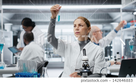 Medical lab technician investigates blue liquid chemical sample properties in test tube. Research facility worker holds vial containing new compound, doing medical RD, camera B Medical lab technician investigates blue liquid chemical sample properties in test tube. Research facility worker holds vial containing new compound, doing medical RD, camera B 142646883