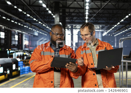 Multiethnic personnel using devices to manage steel production tasks, surrounded by metal machinery and fabrication tools. Professional engineering and manpower on the factory floor. Multiethnic personnel using devices to manage steel production tasks, surrounded by metal machinery and fabrication tools. Professional engineering and manpower on the factory floor. 142646901