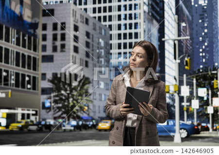 Businesswoman holding tablet traversing city blocks to reach office building. Corporate worker walking on metropolitan avenue to job location, using digital touchscreen device 142646905