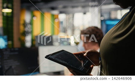 Close up of IT professional in startup office working on tablet with AI driving market innovation. Tech agency admin uses device to optimize operations with neural network, camera A Close up of IT professional in startup office working on tablet with AI driving market innovation. Tech agency admin uses device to optimize operations with neural network, camera A 142646906