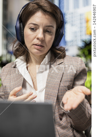Talking in remote call, laptop and woman wearing headphones sitting on park bench. Chatting with coworker, notebook and freelancer outdoors in videoconference, embracing digital nomad lifestyle Talking in remote call, laptop and woman wearing headphones sitting on park bench. Chatting with coworker, notebook and freelancer outdoors in videoconference, embracing digital nomad lifestyle 142646907