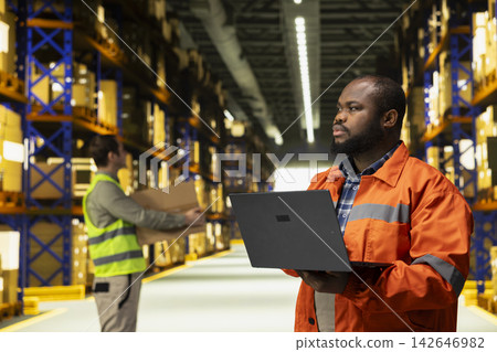 Black male staff organizing cargo packages in fulfillment center facility, warehouse workforce maintains safety and efficiency with pallets distribution through logistics tracking systems. Black male staff organizing cargo packages in fulfillment center facility, warehouse workforce maintains safety and efficiency with pallets distribution through logistics tracking systems. 142646982