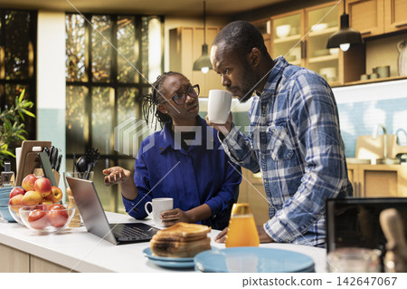 African american wife and husband making a delicious morning meal, checking laptop for recipe on countertop. Sharing laugher and joy over morning coffee, healthy adult lifestyle with fresh food. African american wife and husband making a delicious morning meal, checking laptop for recipe on countertop. Sharing laugher and joy over morning coffee, healthy adult lifestyle with fresh food. 142647067