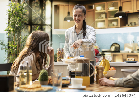 Mother preparing packed lunch in box for her daughter at school, family serving breakfast early in the morning. Back to school meal prep with sandwich and fruits, morning routine. Mother preparing packed lunch in box for her daughter at school, family serving breakfast early in the morning. Back to school meal prep with sandwich and fruits, morning routine. 142647074