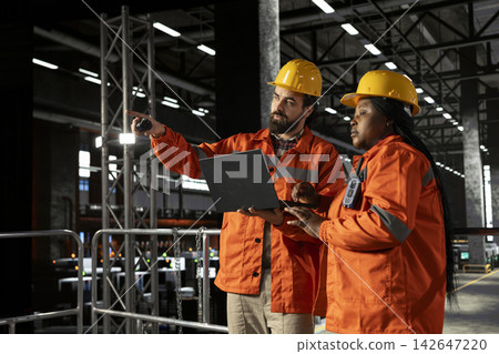 Diverse engineers team using walkie-talkie communication in large-scale factory, radio signal communication ensuring efficient machinery hall operations for production line and steel work. Diverse engineers team using walkie-talkie communication in large-scale factory, radio signal communication ensuring efficient machinery hall operations for production line and steel work. 142647220