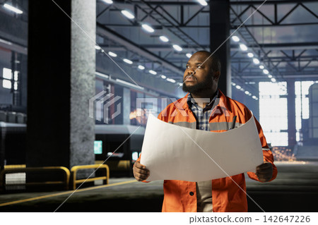 Black supervisor in a factory inspecting machinery plans for production tasks, metal industry production via professional engineering. Industrial workflow essential to steel manufacturing. Black supervisor in a factory inspecting machinery plans for production tasks, metal industry production via professional engineering. Industrial workflow essential to steel manufacturing. 142647226