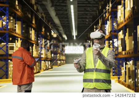 Professional adult male exploring metaverse training program in fulfillment center. VR headset provides immersive experience for package handling and e-commerce distribution workflow. Professional adult male exploring metaverse training program in fulfillment center. VR headset provides immersive experience for package handling and e-commerce distribution workflow. 142647232