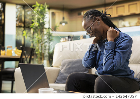 African american freelancer stretching neck and upper back muscles at home, discomfort due to sedentary life and bad pose on sofa. Experiencing stiffness and cramps, physical fatigue. African american freelancer stretching neck and upper back muscles at home, discomfort due to sedentary life and bad pose on sofa. Experiencing stiffness and cramps, physical fatigue. 142647357