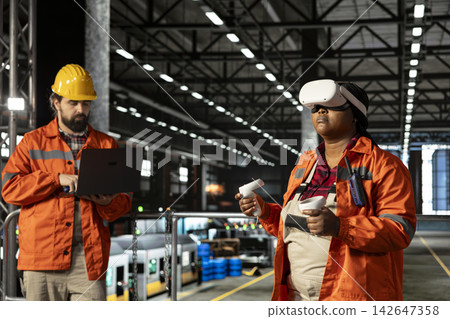 African american woman uses VR headset for interactive monitoring of machinery, immersive 3D simulation helping production line and manufacturing process. Large-scale engineering plant. African american woman uses VR headset for interactive monitoring of machinery, immersive 3D simulation helping production line and manufacturing process. Large-scale engineering plant. 142647358