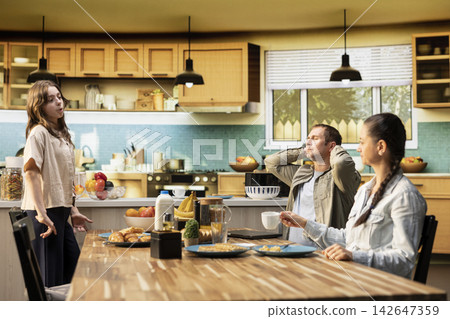 Father relaxing and sitting laid back at the breakfast table after finishing his tasks on laptop, taking a break to enjoy morning routine with his tween daughter and wife. Coffee and pastry. Father relaxing and sitting laid back at the breakfast table after finishing his tasks on laptop, taking a break to enjoy morning routine with his tween daughter and wife. Coffee and pastry. 142647359