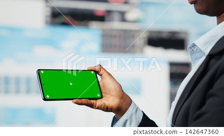Manager using isolated screen smartphone to compare company metrics on digital videowall before making decisions. Entrepreneur analyzing key performance indicators using mockup phone, camera B Manager using isolated screen smartphone to compare company metrics on digital videowall before making decisions. Entrepreneur analyzing key performance indicators using mockup phone, camera B 142647360
