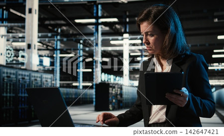 Data center female admin uses devices and AR simulation to conduct security audit on equipment rigs. Woman in server farm uses digital twin scan virtualization to verify firewall protection Data center female admin uses devices and AR simulation to conduct security audit on equipment rigs. Woman in server farm uses digital twin scan virtualization to verify firewall protection 142647421