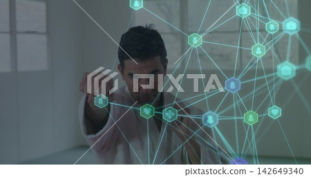 Striking adult male karate student wearing white gi punching in bright dojo, with digital overlay Striking adult male karate student wearing white gi punching in bright dojo, with digital overlay 142649340