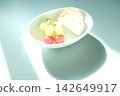 Light and shadow: Grapes, cherries, and a selection of bread in a white container. 142649917